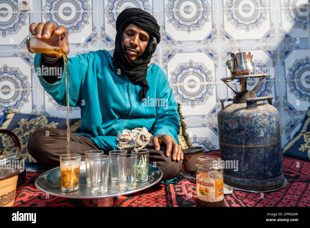 Berbère vêtu de djellaba et de turban noir servant du thé de façon traditionnelle. Banque D'Images
