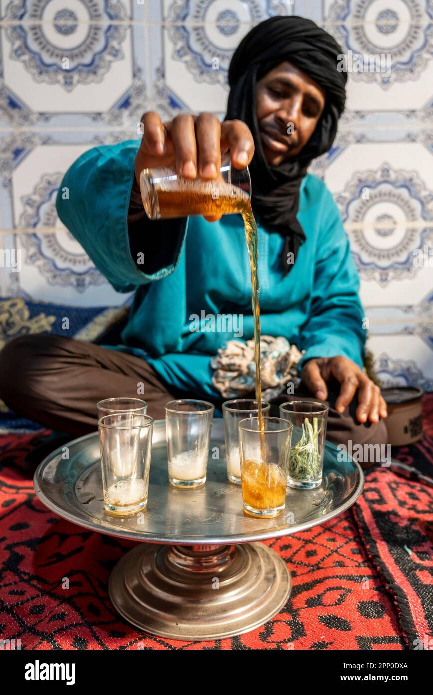 Berbère vêtu de djellaba et de turban noir servant du thé de façon traditionnelle. Banque D'Images