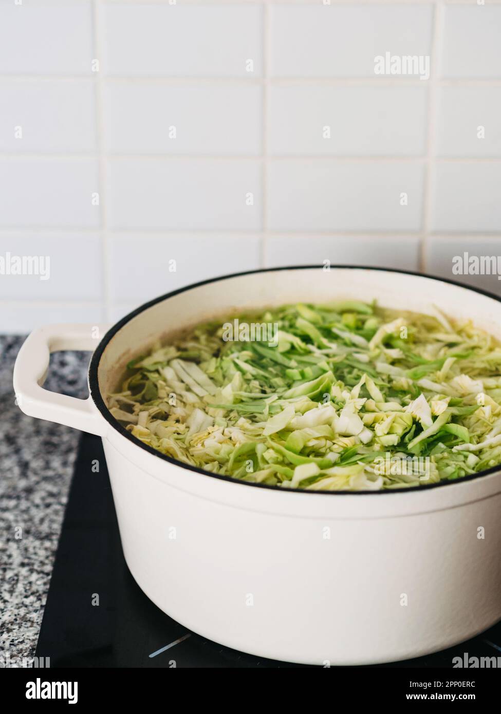 Poêle blanche en céramique avec chou haché dans un bouillon sur la cuisinière. Étape de préparation de la soupe aux légumes Banque D'Images