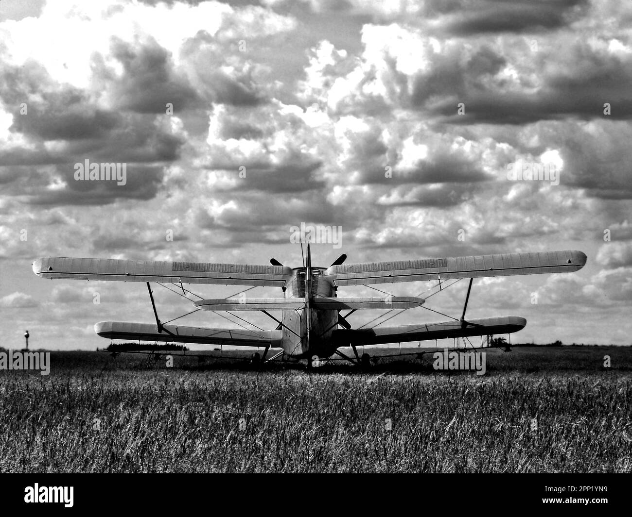 vieux biplan isolé sur un aérodrome de prairie sombre sous un ciel dynamique avec des nuages blancs vus de l'arrière. image en noir et blanc. vol de planeur. Banque D'Images