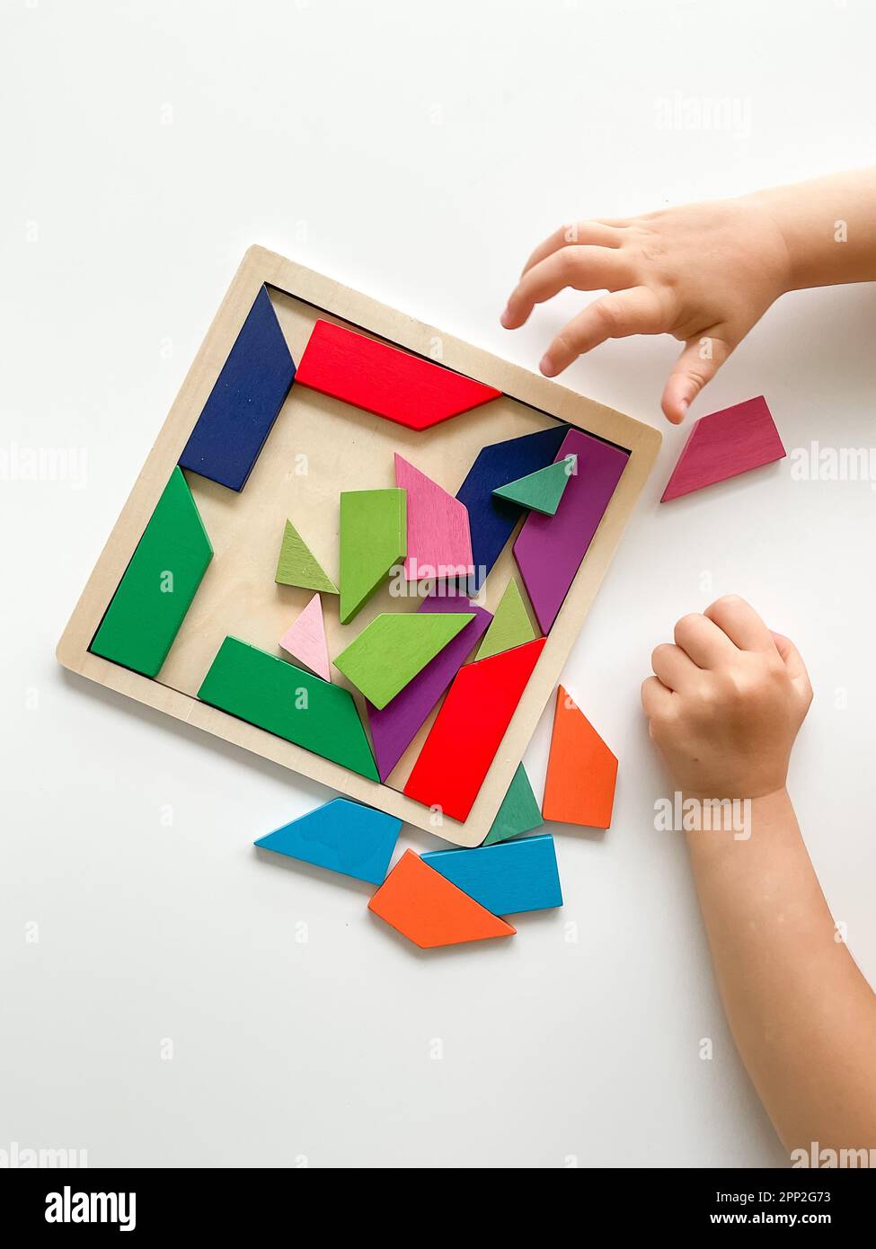 la main de childs recueille la mosaïque en bois multicolore sur fond blanc. Banque D'Images