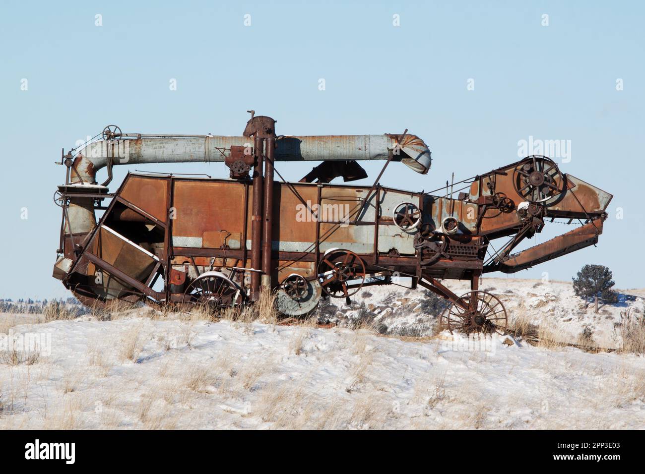 Une machine de battage ancienne abandonnée ressemble à un lézard métallique sur une pente enneigée dans les plaines du Montana Banque D'Images