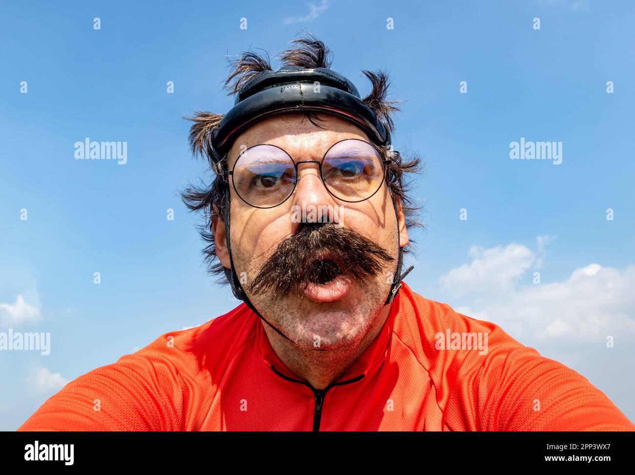 Un cycliste émotionnel conduit sur un vélo dans un casque rétro sous un ciel bleu Banque D'Images