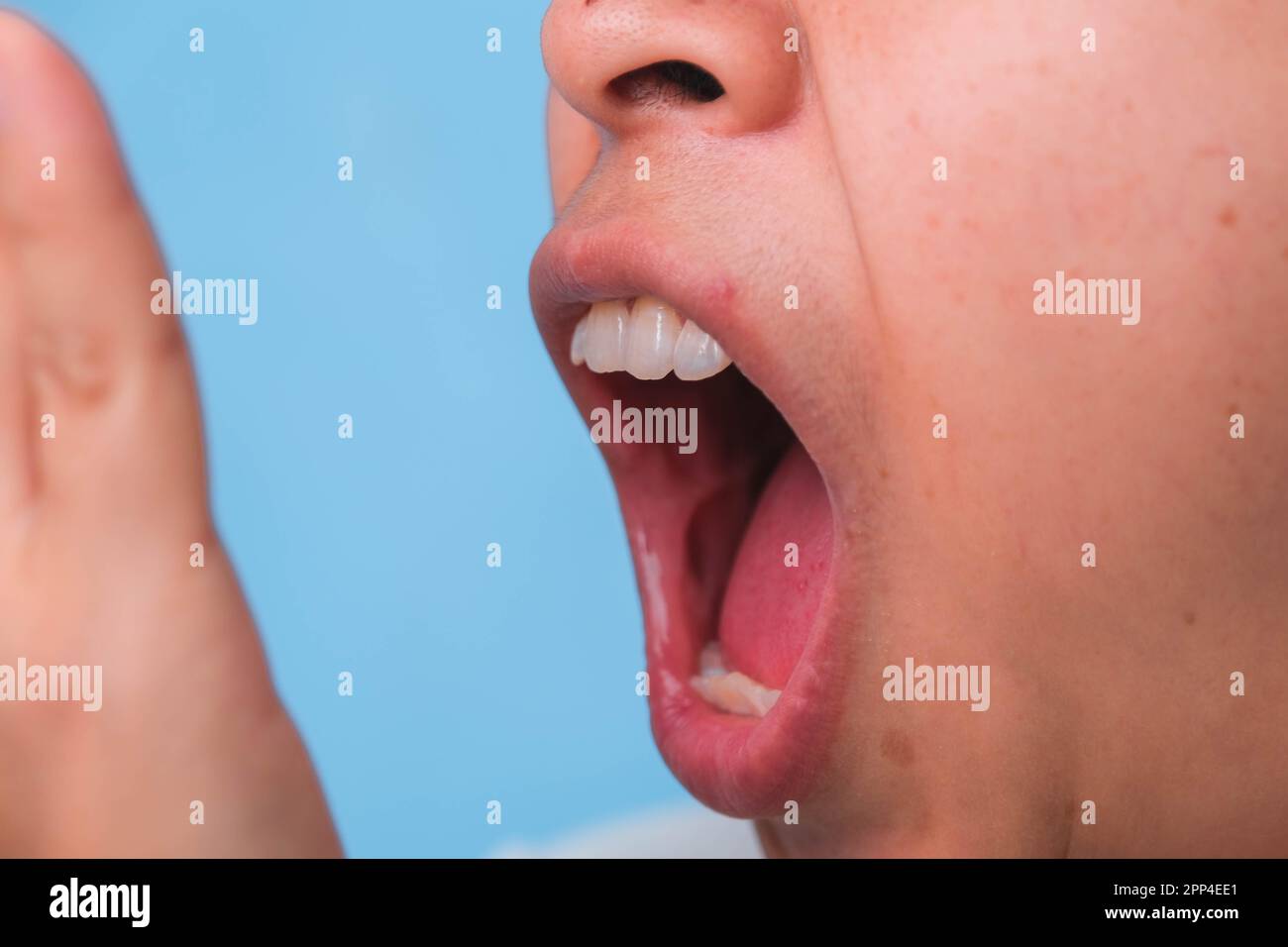 Femme couvrant sa bouche pour sentir la mauvaise haleine. Une jeune femme qui vérifie sa respiration avec ses mains. Problèmes de santé bucco-dentaire ou concept de soins dentaires. Banque D'Images