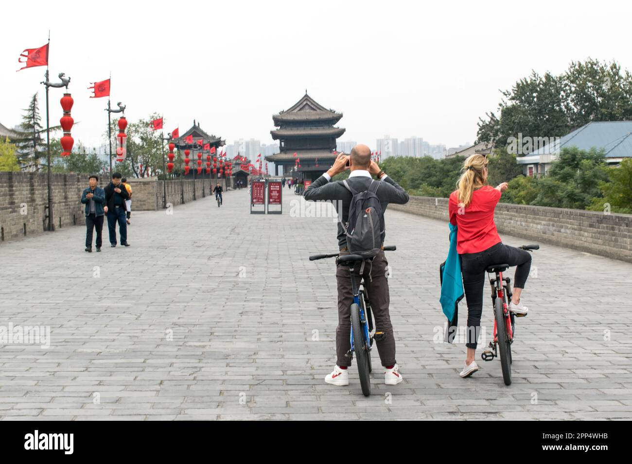 Le dos de deux touristes, un homme et une femme, s'arrêtent sur le mur de la ville de Xi'an tout en vélo pour prendre une photo. Banque D'Images