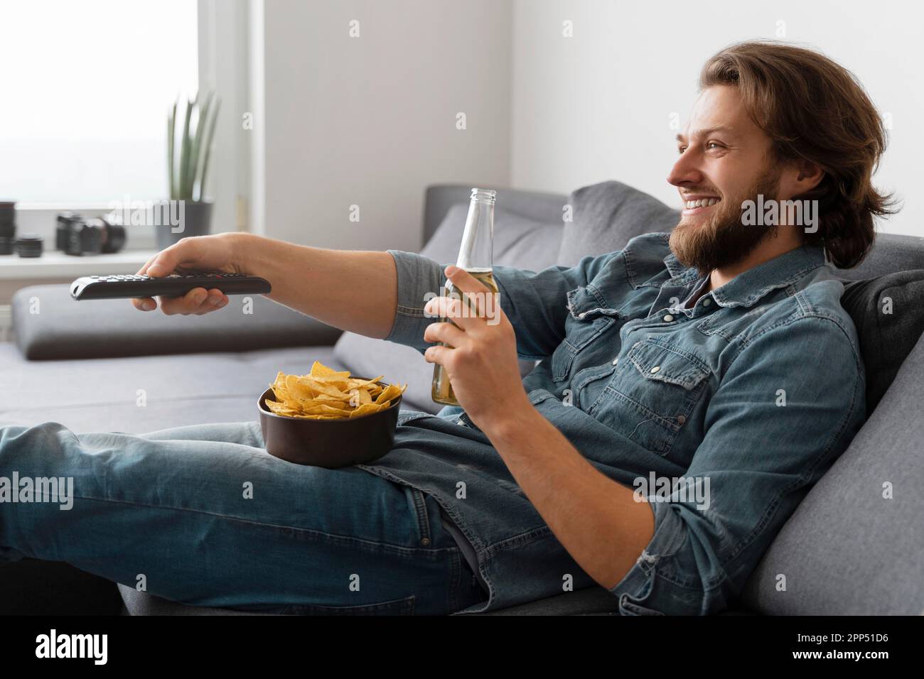 Homme de taille moyenne avec boisson regardant la télévision Banque D'Images