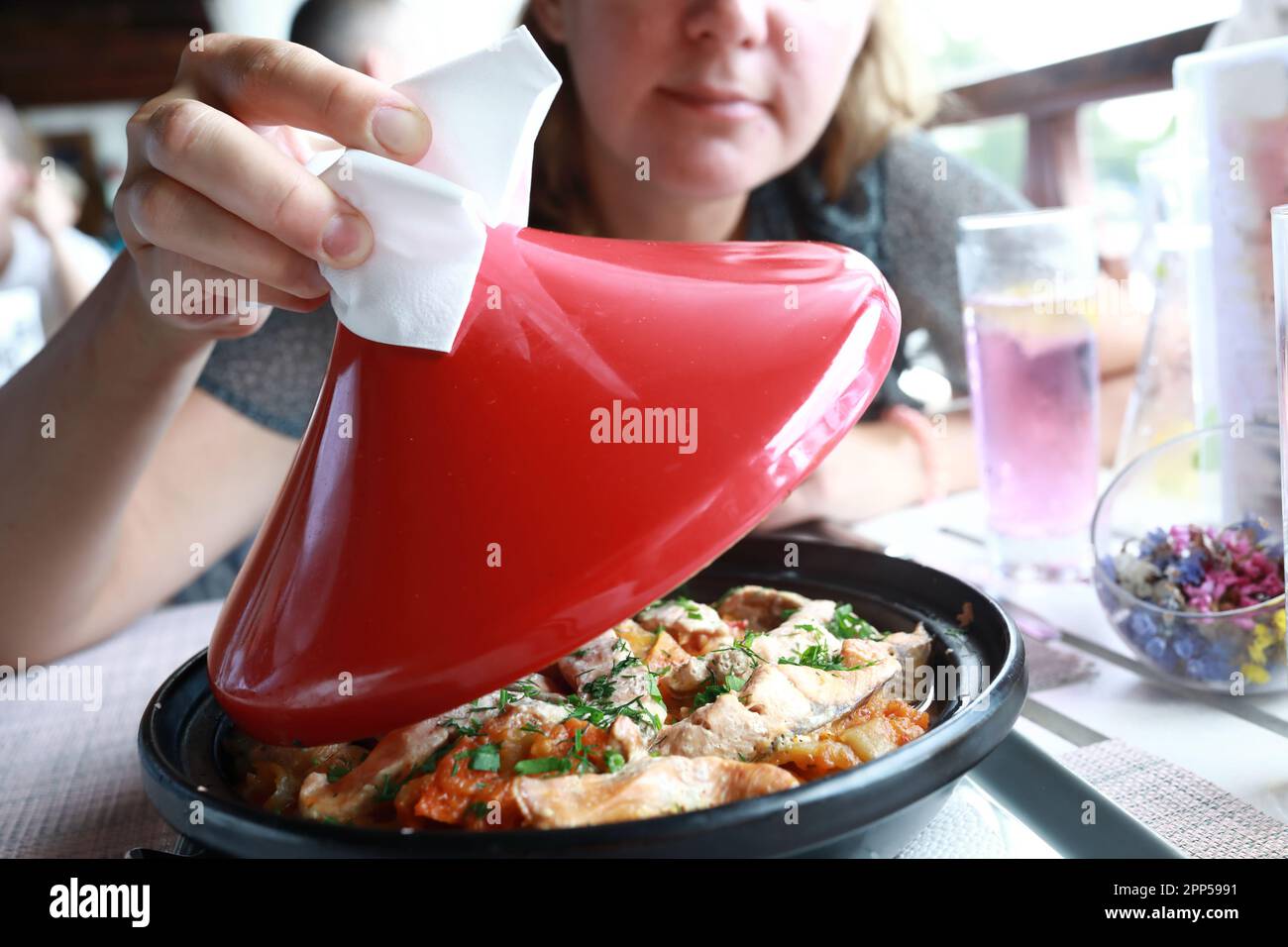 Femme soulevant le couvercle rouge de tagine dans le restaurant Banque D'Images