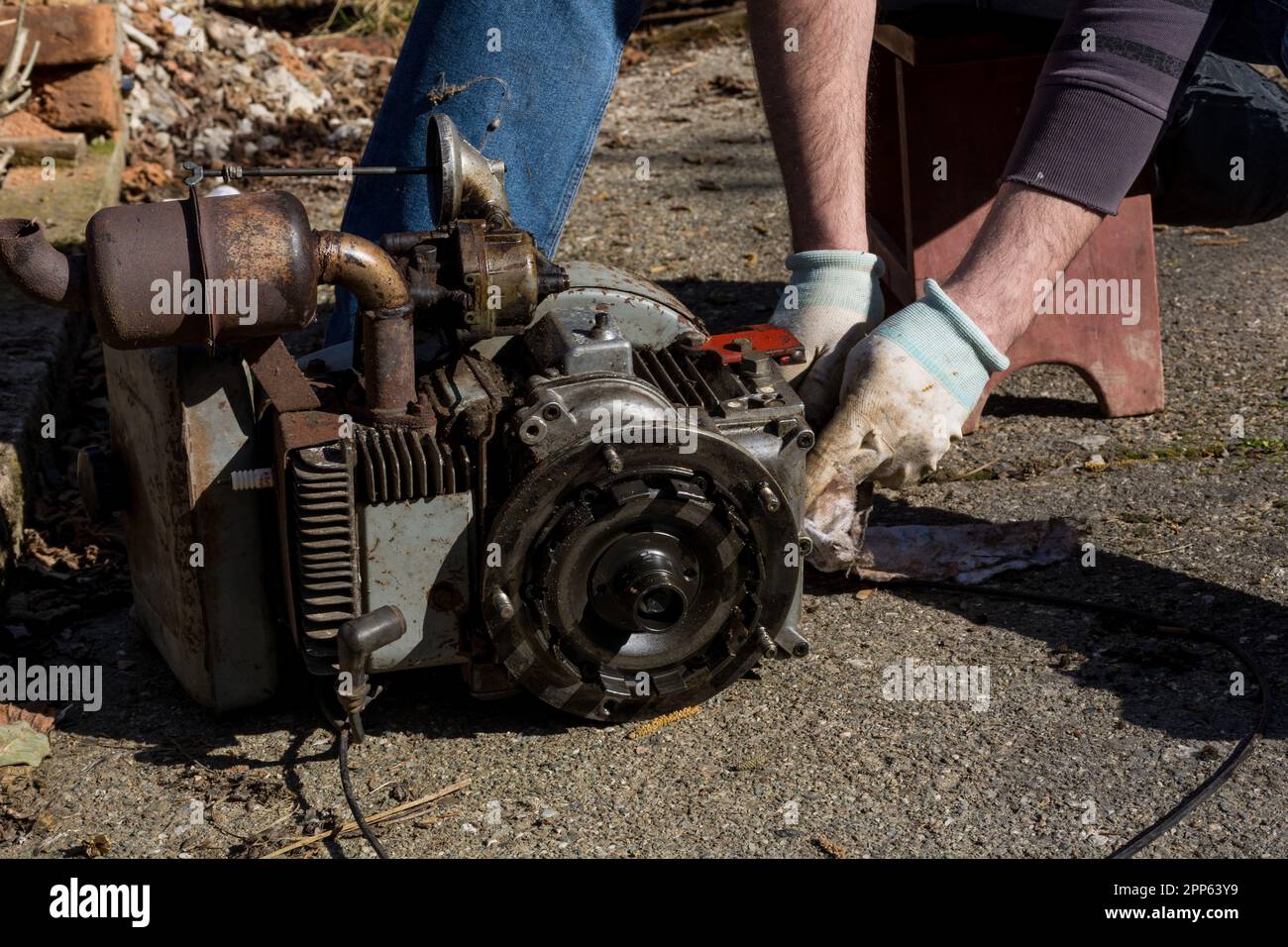 Le mécanicien fixe un ancien moteur d'un cultivateur. Il est assis sur une  chaise et démonte le moteur, l'entretient avec ses mains Photo Stock - Alamy