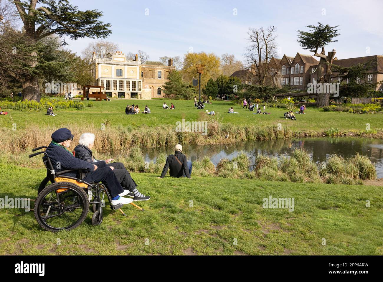 Couple âgé, dont un handicapé en fauteuil roulant, assis dans un parc au printemps; Walpole Park, Ealing, Londres, Royaume-Uni; - accès handicapés à des espaces publics. Banque D'Images