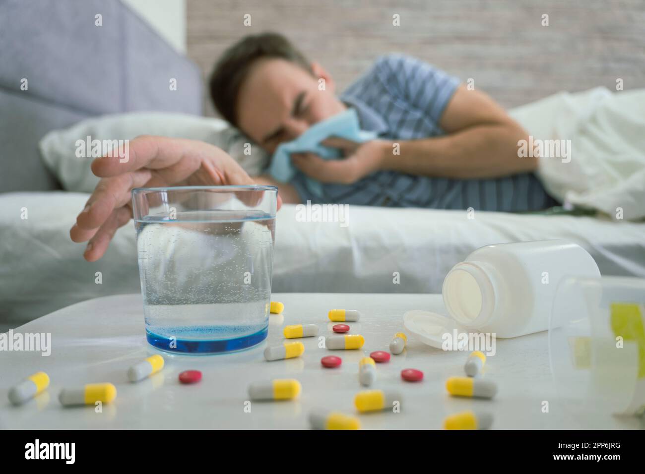 Jeune casien triste et découplé malade mâle se trouve sur le lit sous une couverture, souffre d'écoulement, souffle son nez dans la serviette dans l'intérieur de la chambre blanche. Maladie, fl Banque D'Images