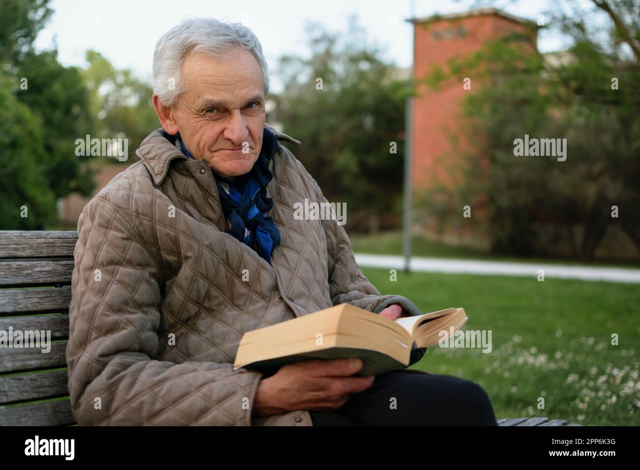 Vieil homme aux cheveux gris lisant un livre placé sur un banc. Banque D'Images