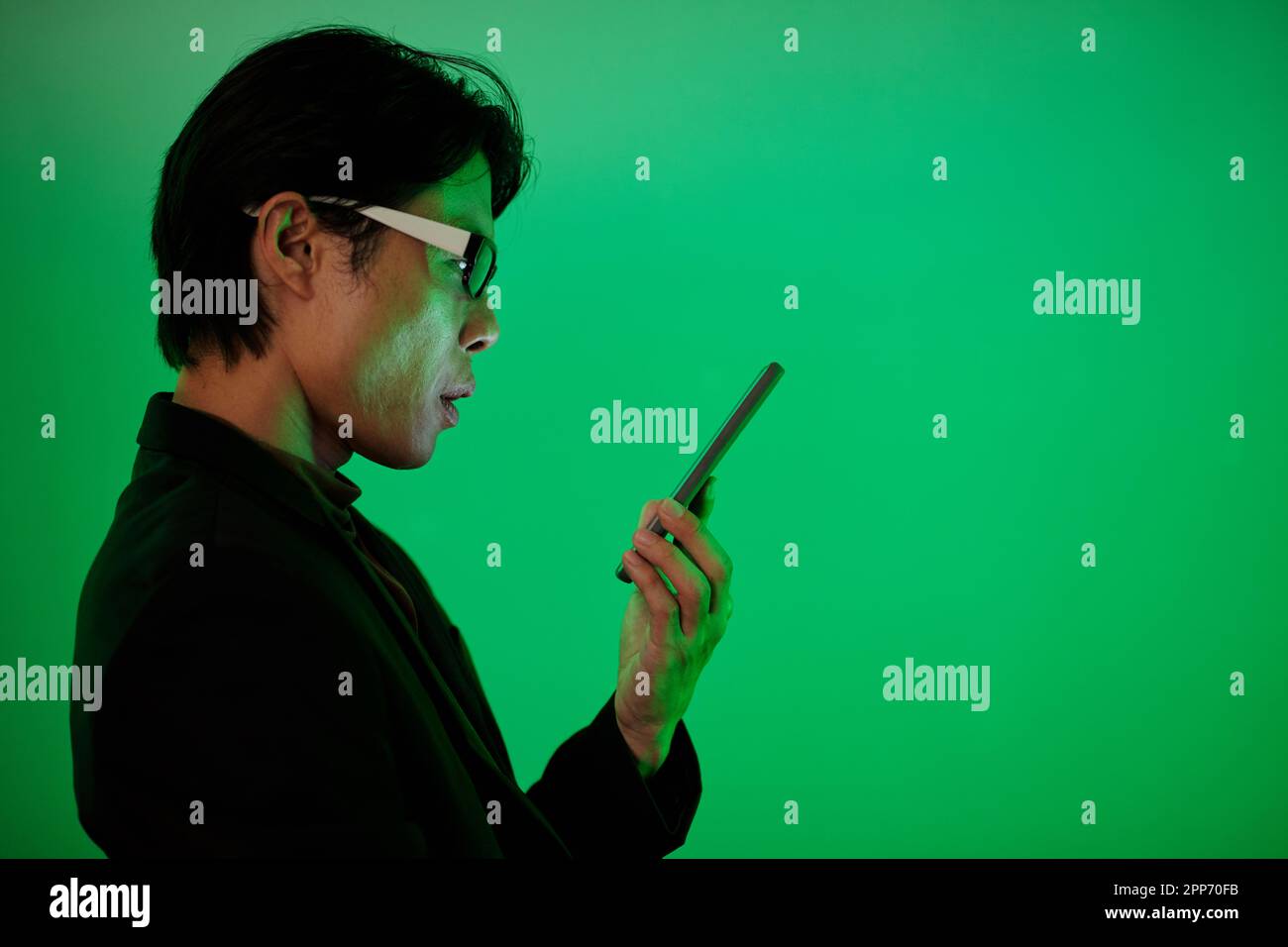 Homme pensif lisant des messages texte dans un smartphone, isolé sur fond vert Banque D'Images
