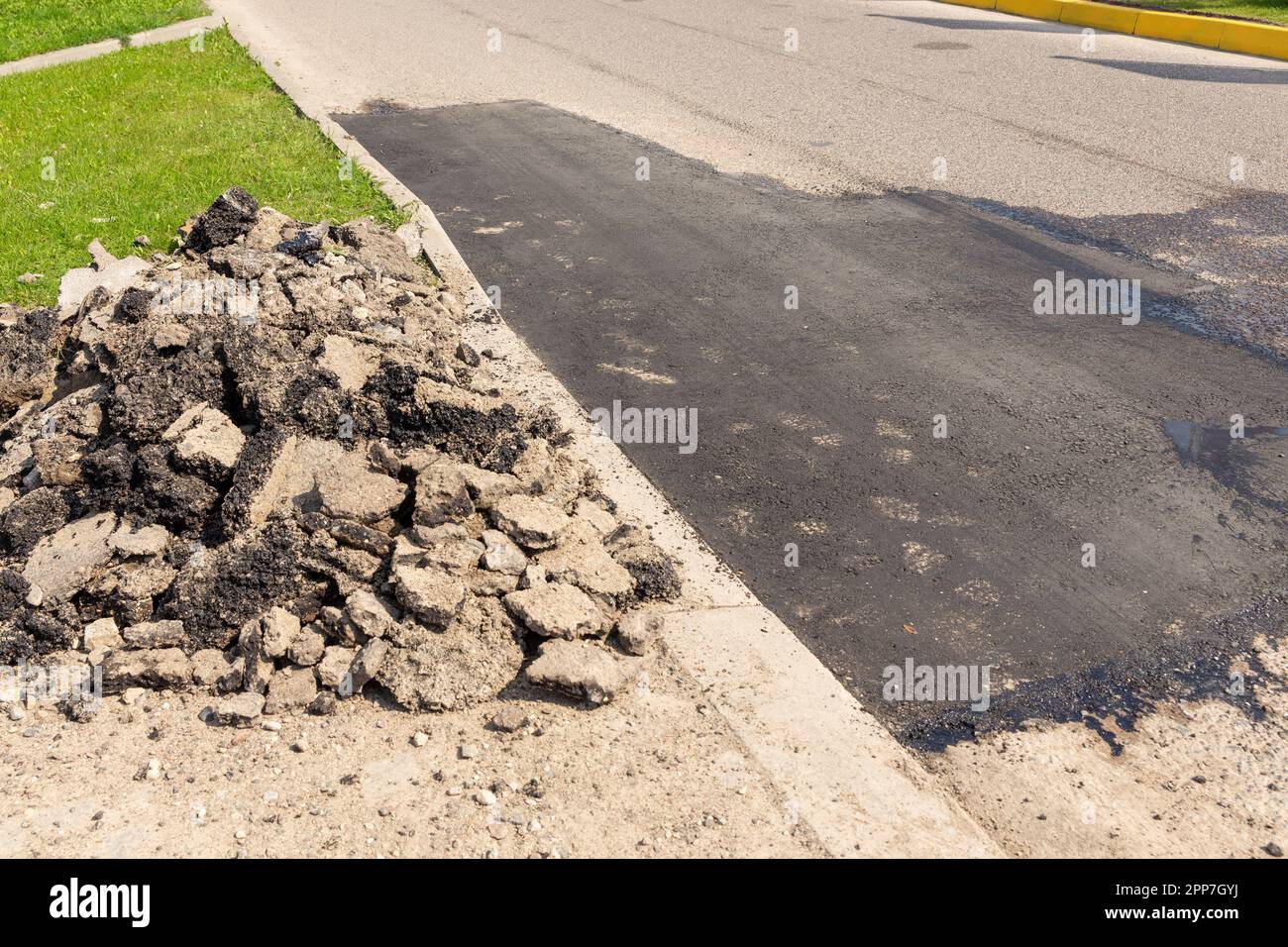 Vue sur une partie fraîchement réparée de la route pavée. Vieux débris de route asphaltée fissurée dégâts de tas sur le sol à recycler. Banque D'Images