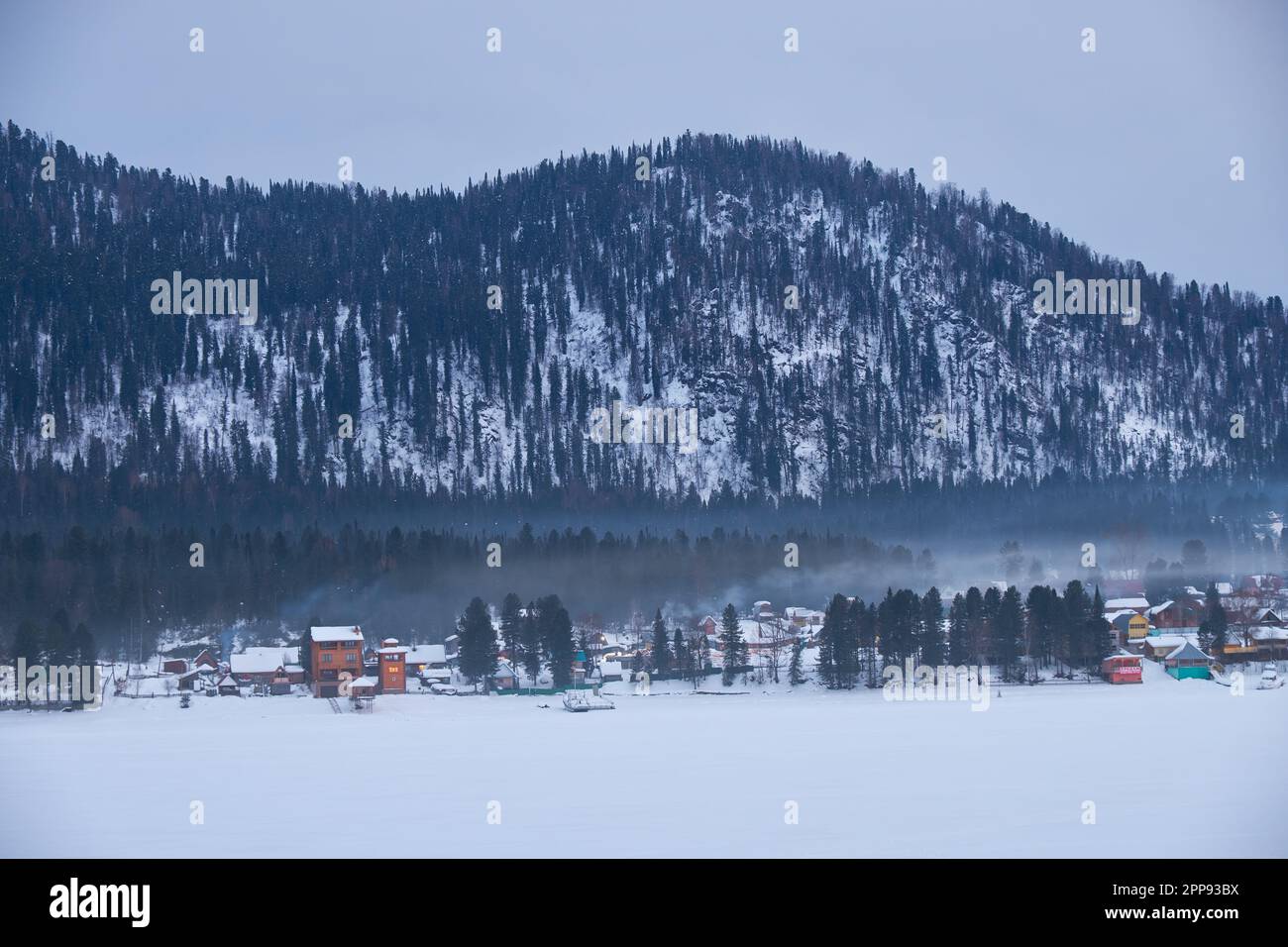 Maisons sur la rive du lac de Teletskoe gelé sous la fumée de cheminée. Iogach, Altaï, Sibérie, Russie Banque D'Images