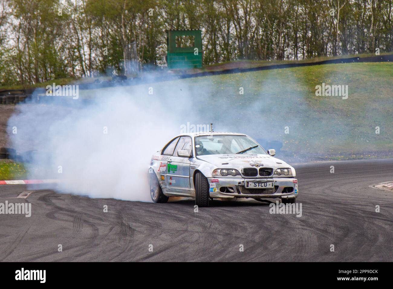 Les voitures de course BMW brûlent du caoutchouc avec des pneus criant au circuit de course de trois Sœurs 3 à Wigan, Lancashire au Royaume-Uni Banque D'Images