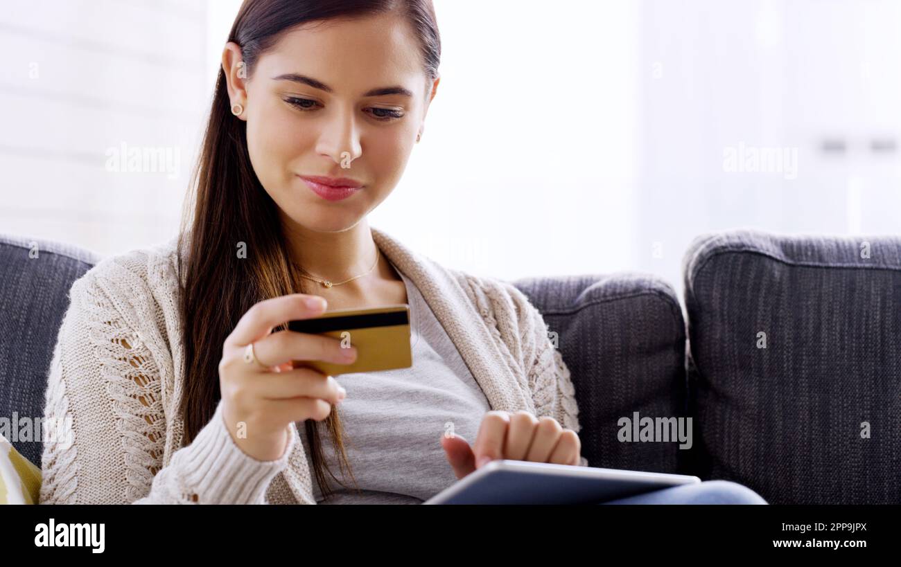 Faire du shopping dans le confort de ma propre maison. une jeune femme attrayante utilisant sa carte de crédit et sa tablette numérique tout en se relaxant sur un canapé à la maison Banque D'Images