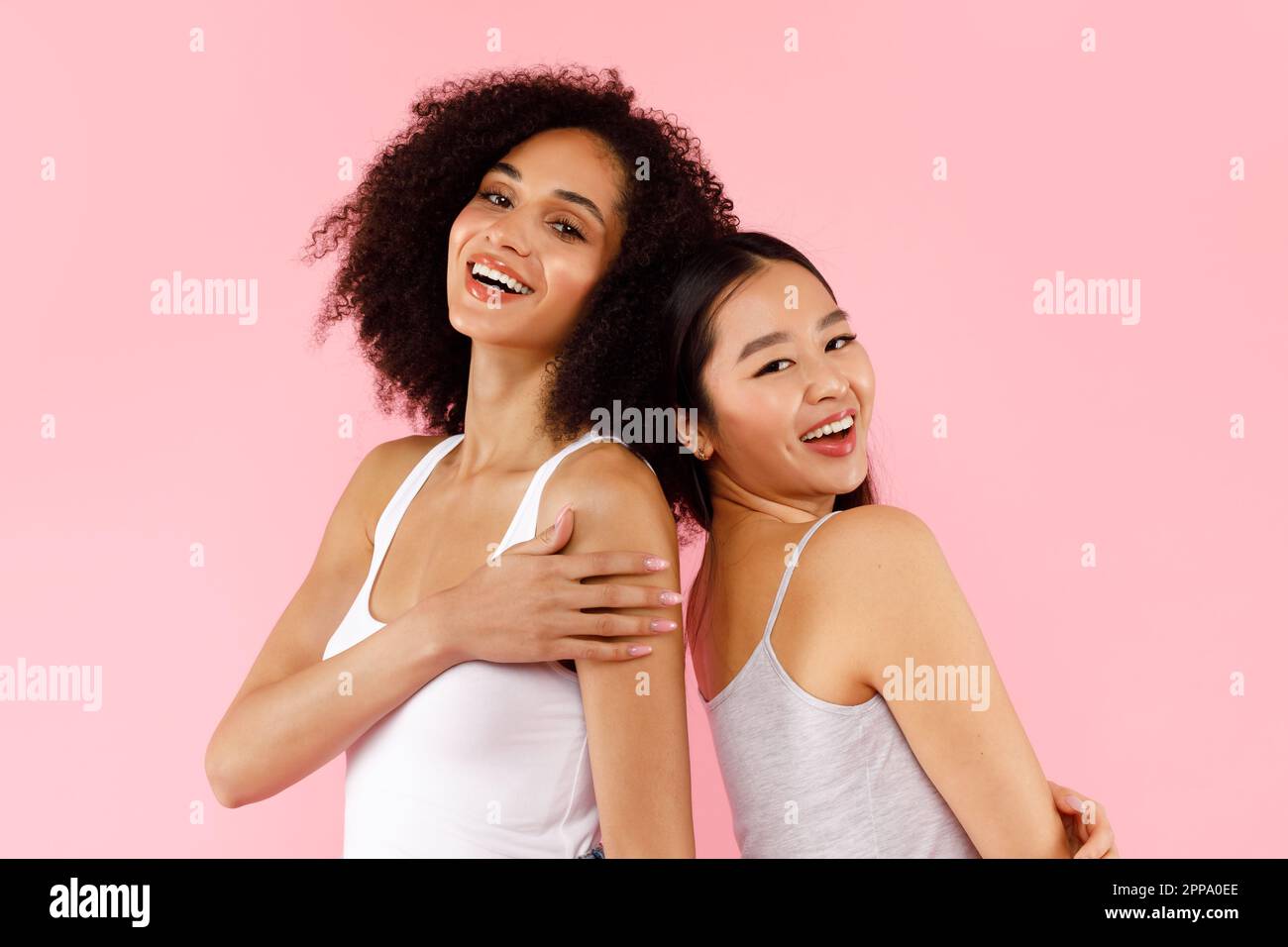 Deux belles femmes africaines américaines et asiatiques posant sur fond rose studio, regardant et souriant à la caméra Banque D'Images