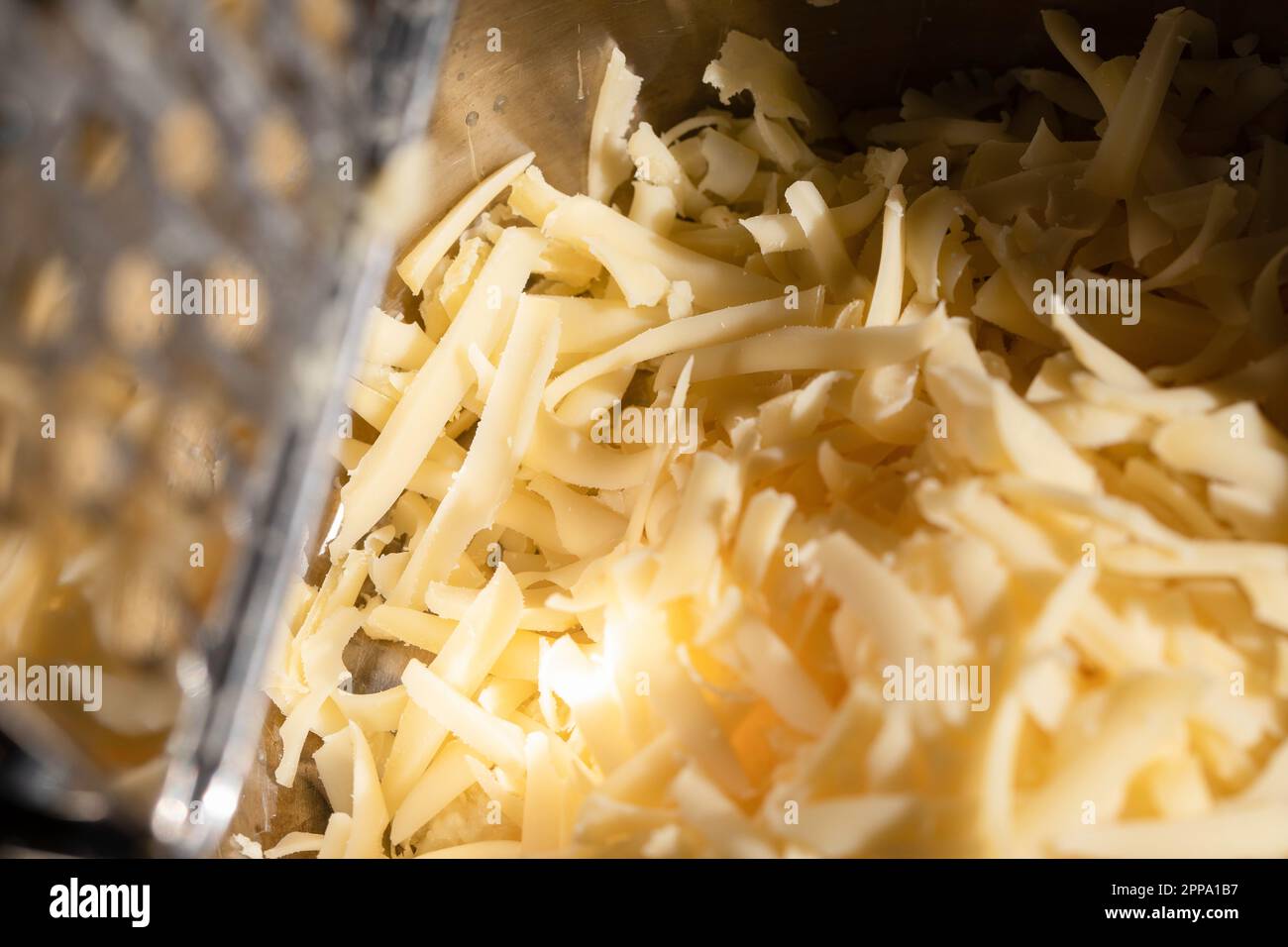 Fromage râpé jaune, matière fondue, râpe à fromage. Banque D'Images