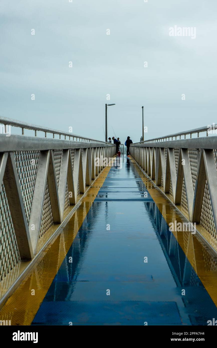 Personnes pêchant à partir d'une jetée par temps pluvieux : une vue en perspective avec des réflexions. Amity point, Stradbroke Island, Queensland, Australie. Banque D'Images