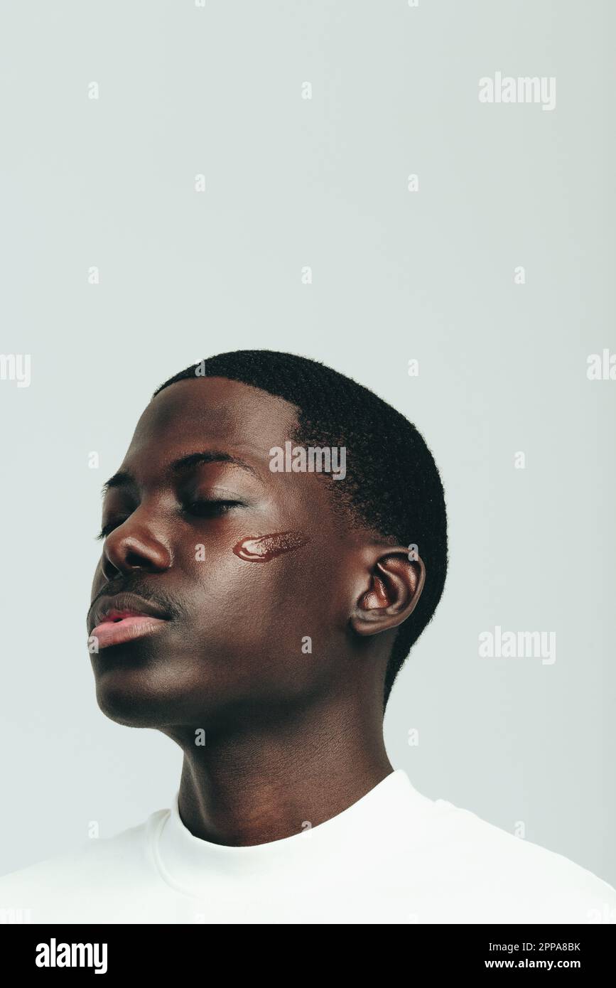Jeune homme noir prenant soin de sa peau de mélanine avec un sérum facial anti-âge dans un studio. Jeune homme confiant pratiquant une beauté saine, marié Banque D'Images