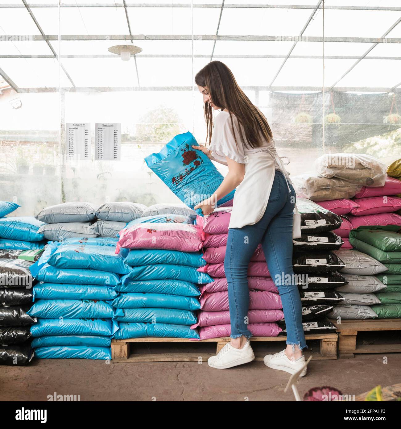 Vue latérale jeune femme souriante empilant des sacs de serre en plastique Banque D'Images