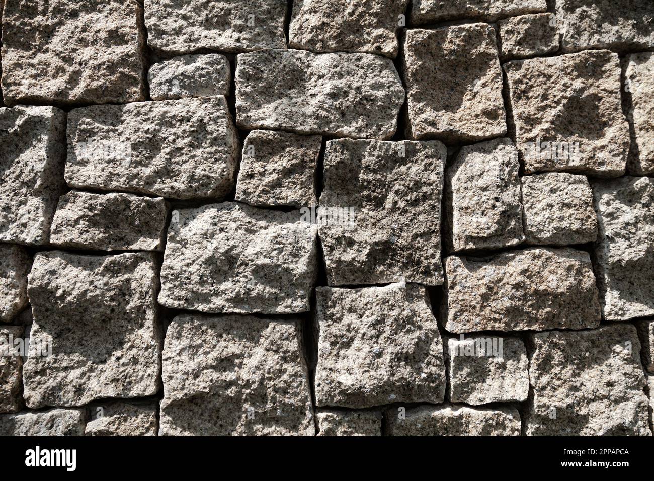 Motif géométrique de fausses pierres décoratives dans un mur. Briques carrées grises posées de manière peu professionnelle avec de grands espaces, arrière-plan Banque D'Images