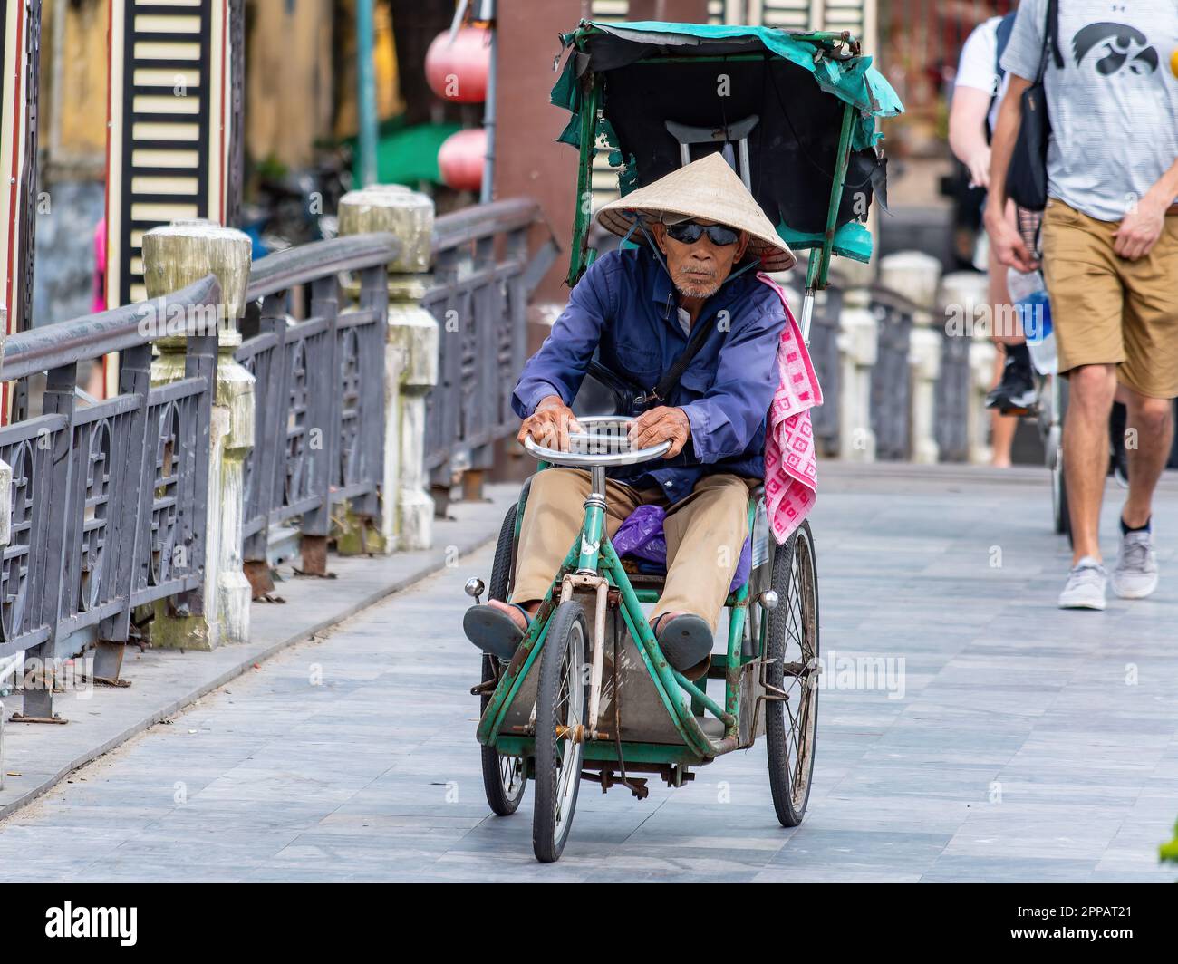 Homme âgé et handicapé traversant un pont sur son tricycle à moteur manuel à Hoi an, province de Quang Nam, Vietnam la nuit. La vieille ville de Hoi an est un culte Banque D'Images