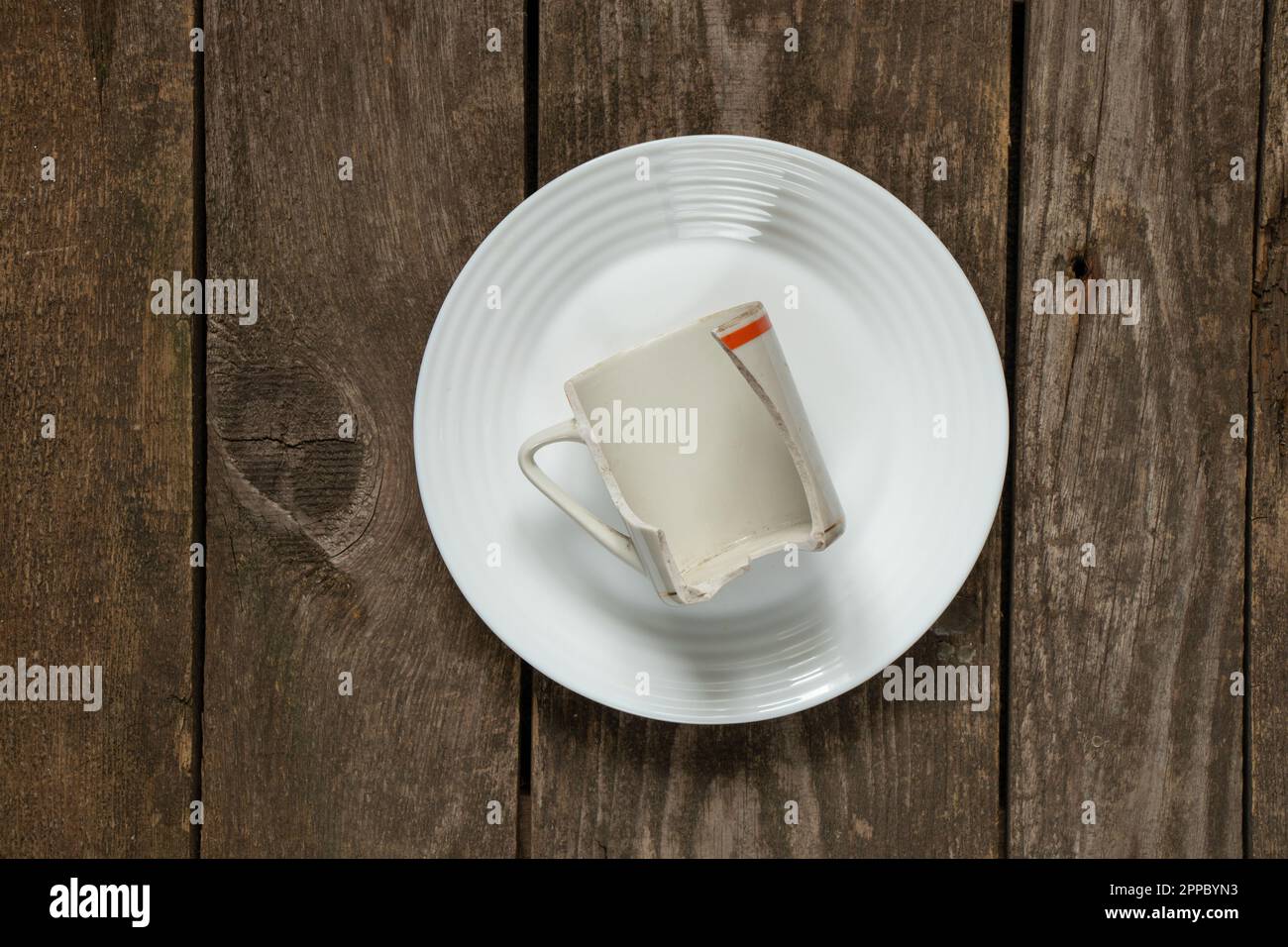 une tasse cassée repose sur une plaque blanche sur une table en bois ancienne, plats cassés Banque D'Images