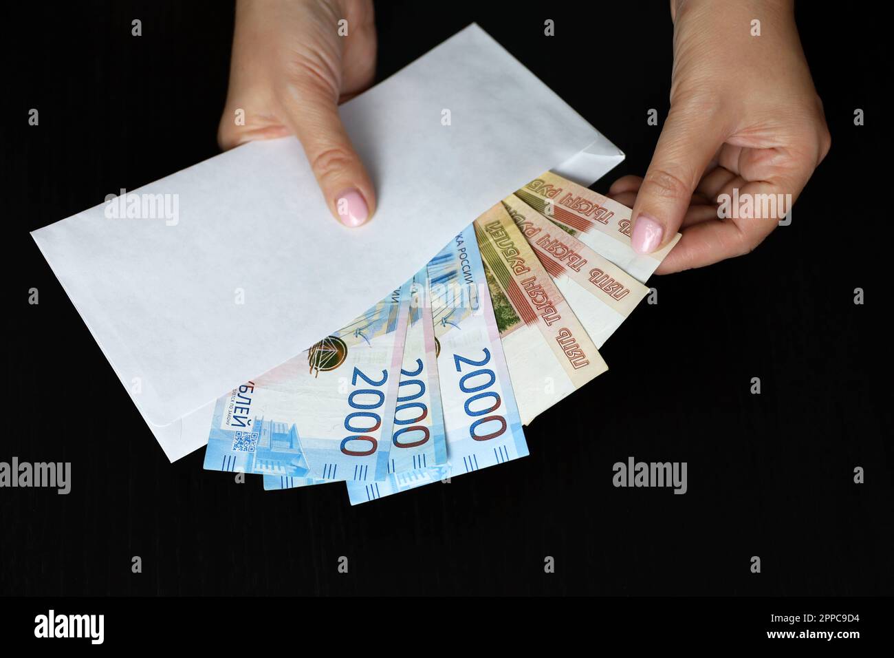 Enveloppe avec roubles russes dans les mains des femmes sur fond noir. Salaires en Russie, concept de bonus ou de pot-de-vin Banque D'Images