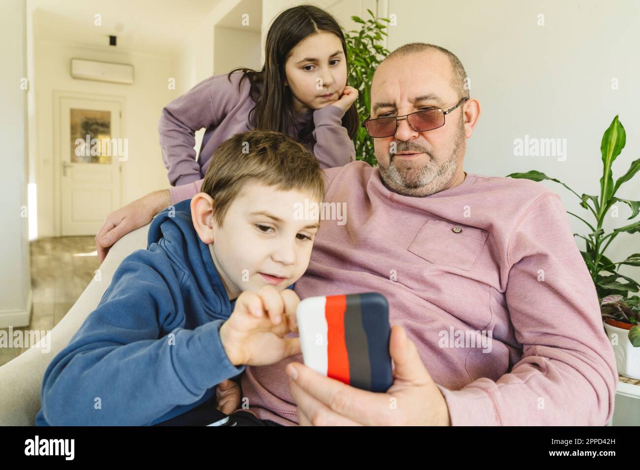 Grand-père partageant un smartphone avec des petits-enfants à la maison Banque D'Images