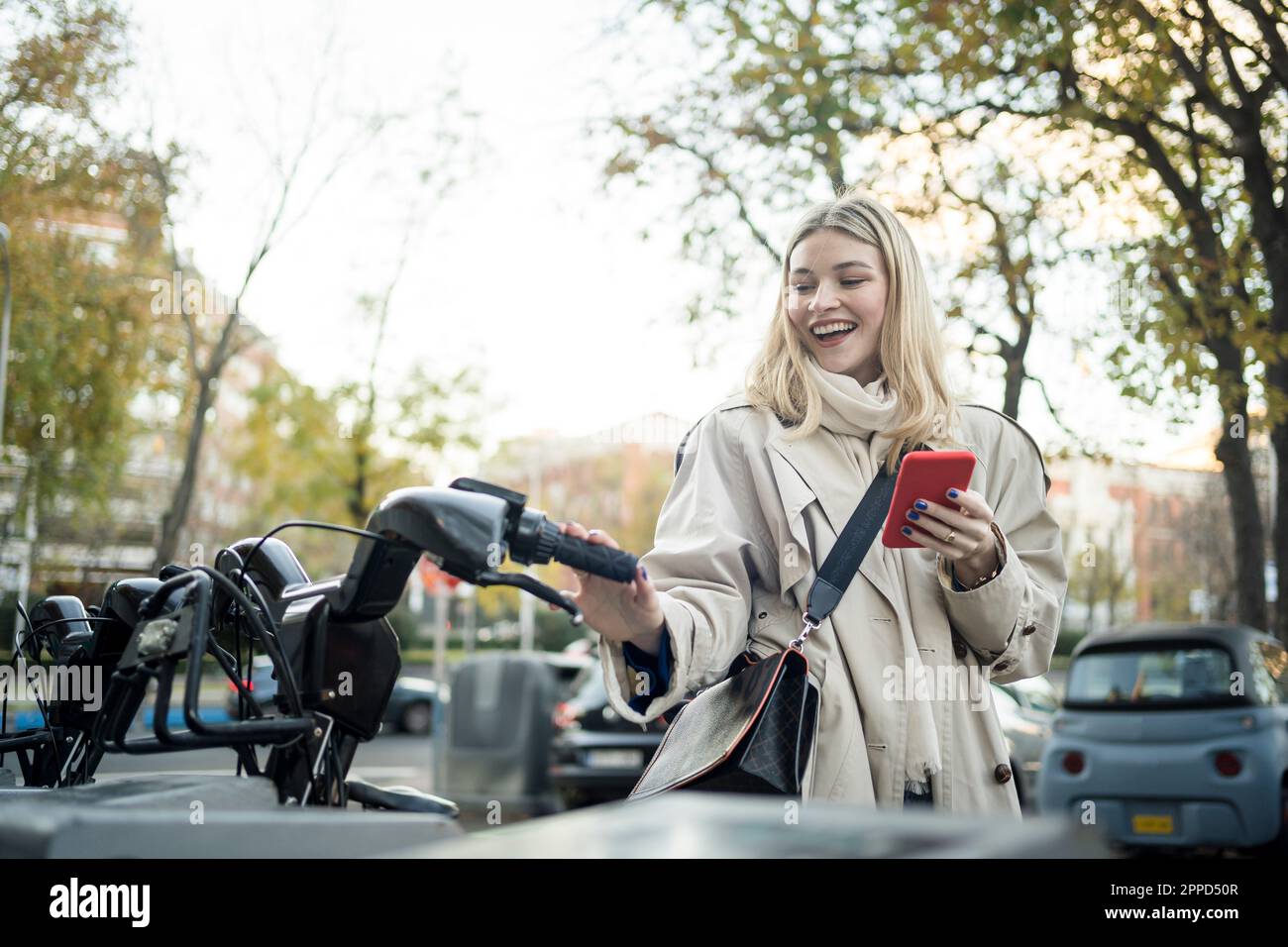 Une femme heureuse avec un smartphone debout à la station de parking pour vélos Banque D'Images