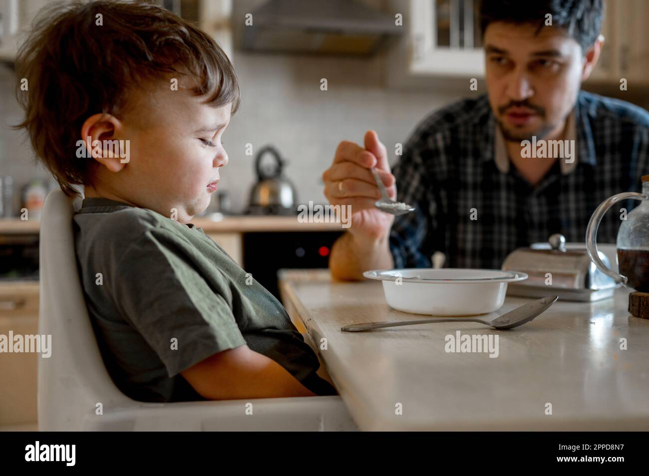Le père nourrissant le fils contrarié assis à la table de salle à manger dans la maison Banque D'Images