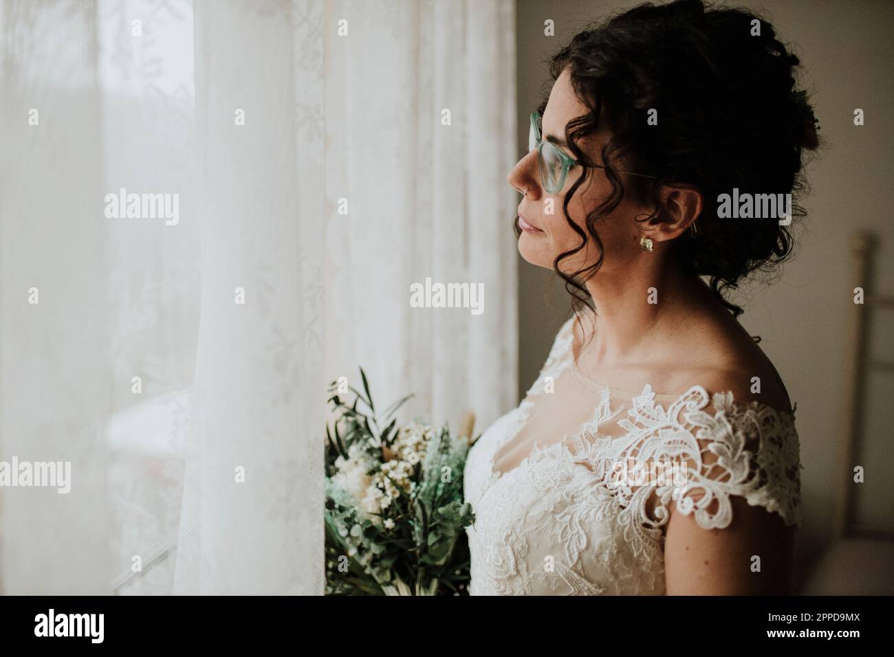 Jeune mariée avec bouquet de vue par la fenêtre Banque D'Images