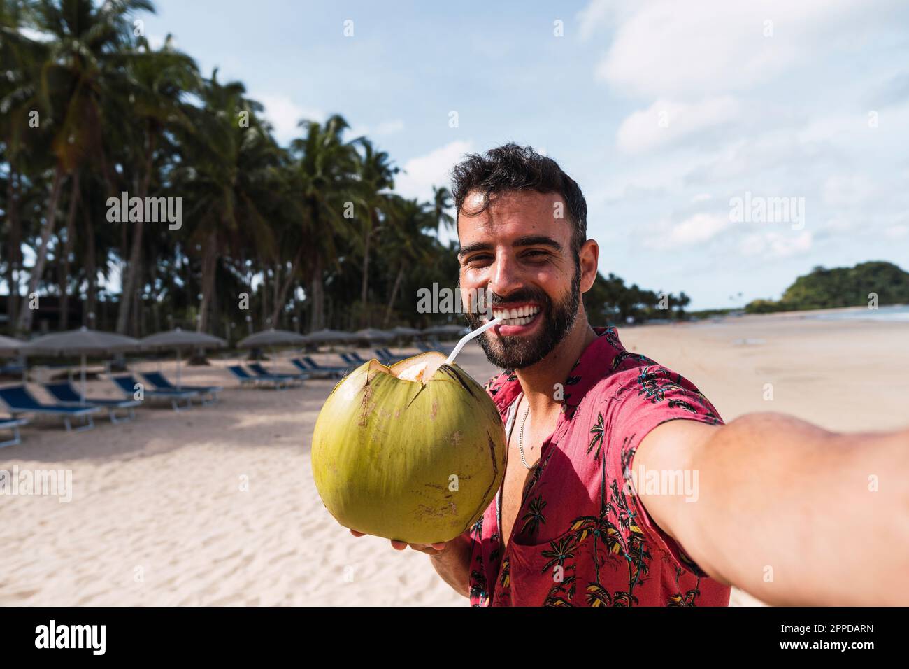Un homme heureux qui boit de l'eau de noix de coco et qui prend le selfie à la plage Banque D'Images