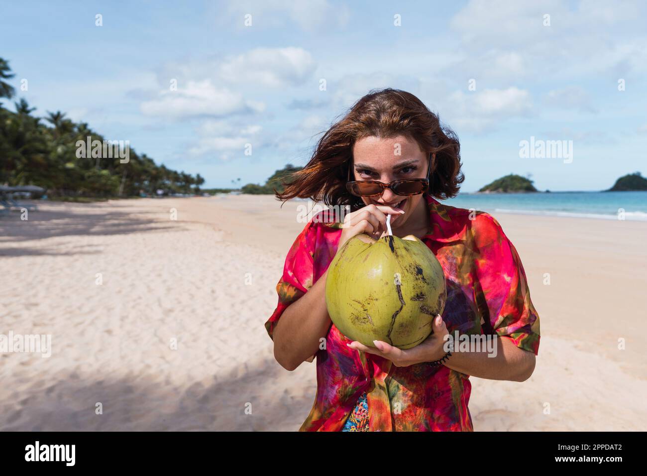 Une jeune femme souriante boit de l'eau de coco à la plage Banque D'Images