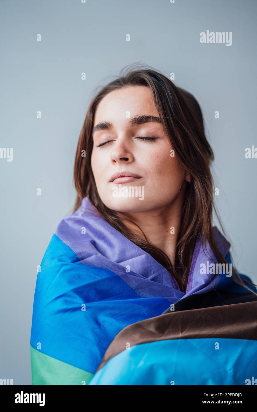 Femme d'affaires avec les yeux fermés enveloppés dans un drapeau arc-en-ciel Banque D'Images