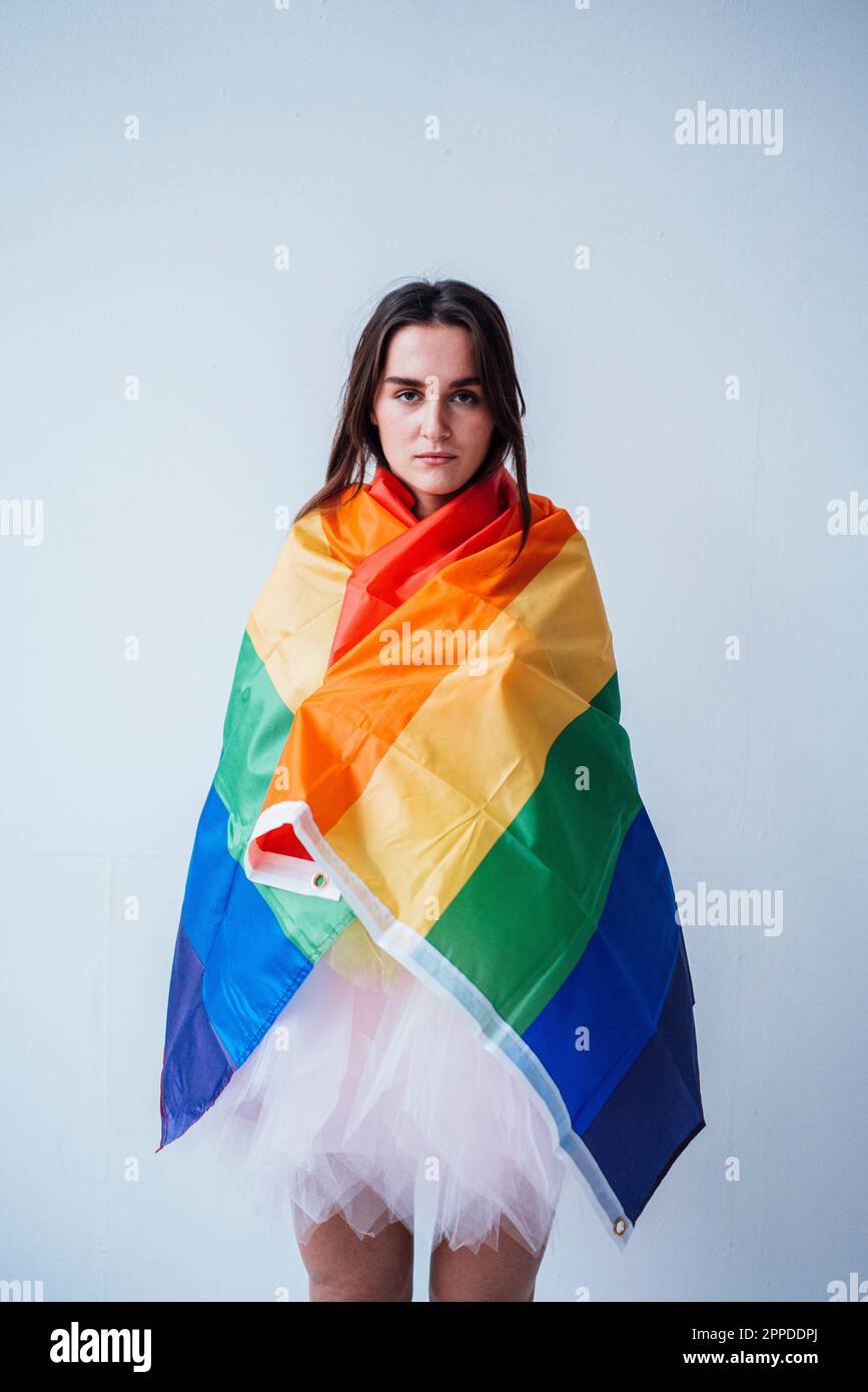 Femme sérieuse couverte d'un drapeau arc-en-ciel debout devant le mur Banque D'Images