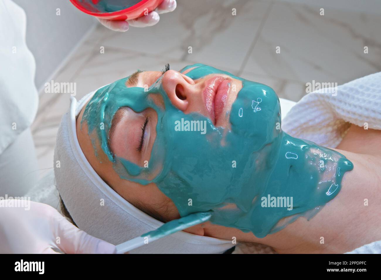 Une esthéticienne appliquant un masque sur le visage d'une jeune femme inclinable dans un salon de beauté pour une procédure de nettoyage et d'hydratation de la peau. Banque D'Images