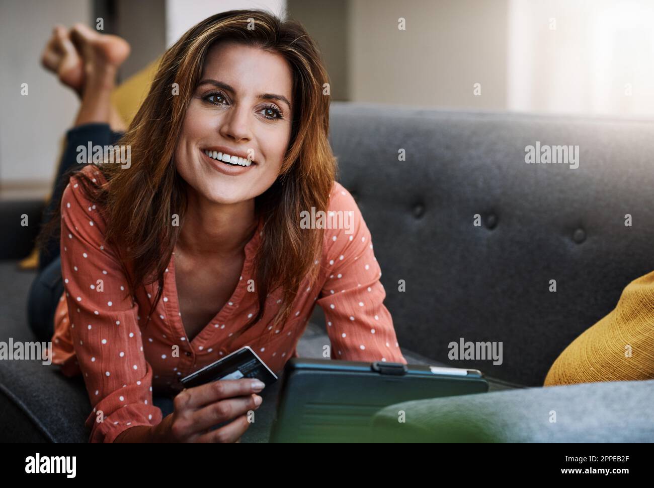Le meilleur des deux mondes, le shopping dans le confort. une jeune femme attrayante utilisant une tablette numérique et une carte de crédit sur le canapé à la maison. Banque D'Images