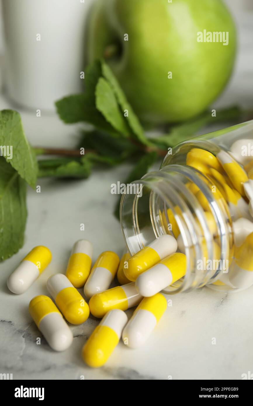 Bouteille avec des pilules de vitamine, des pommes et de la menthe sur table en marbre blanc, gros plan Banque D'Images