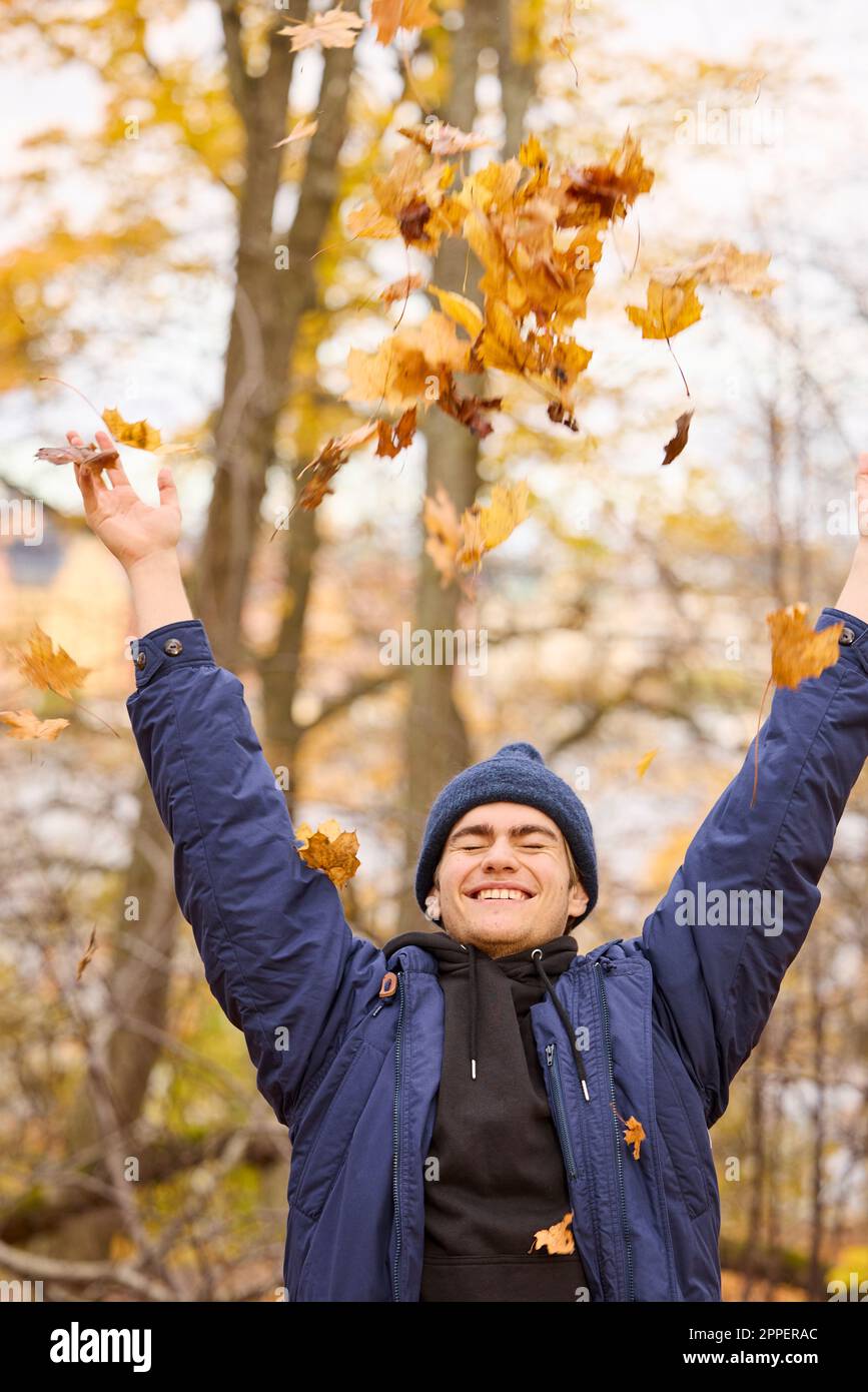 Un jeune homme souriant lance des feuilles d'automne Banque D'Images
