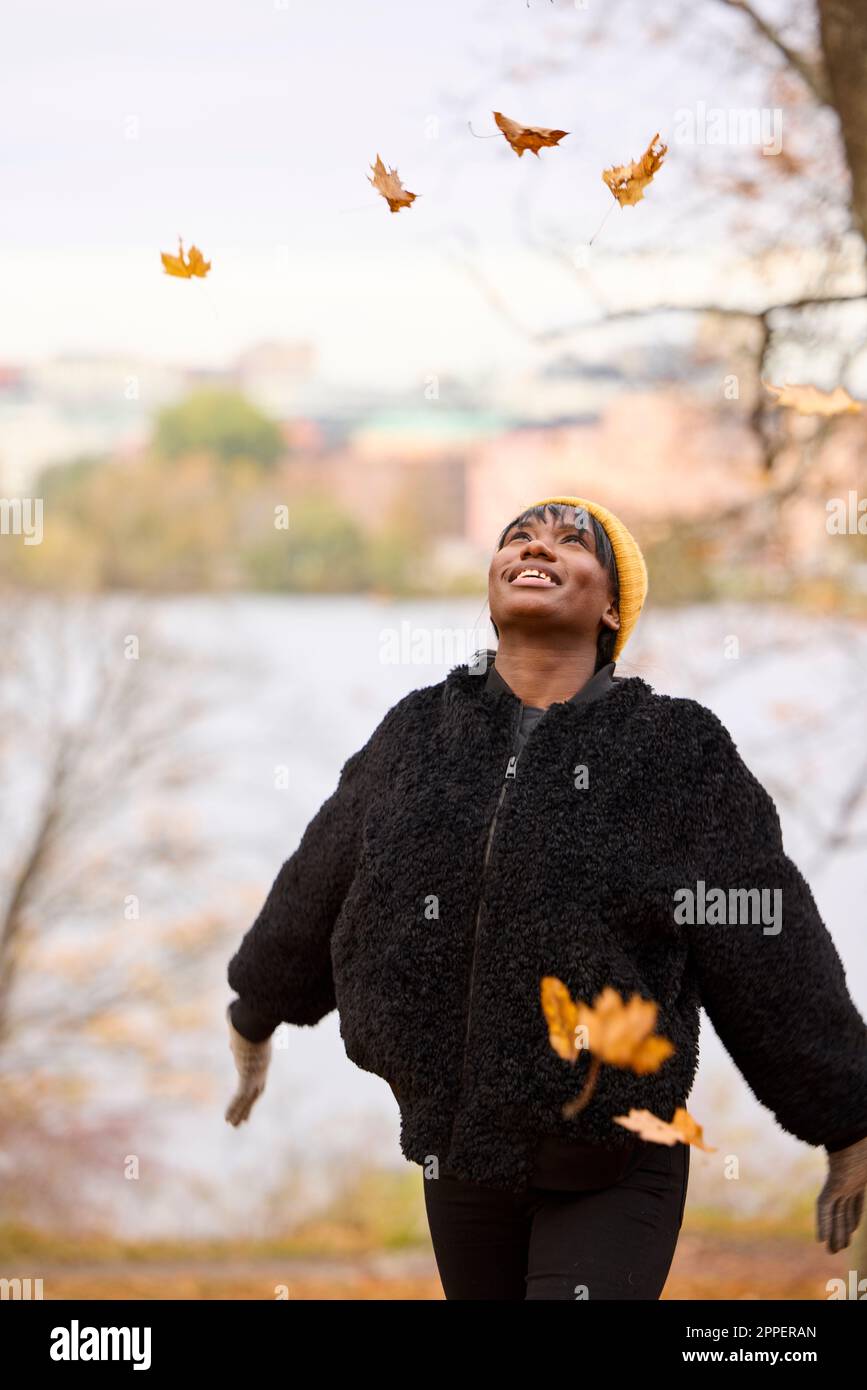 Jeune femme souriante jetant des feuilles d'automne Banque D'Images