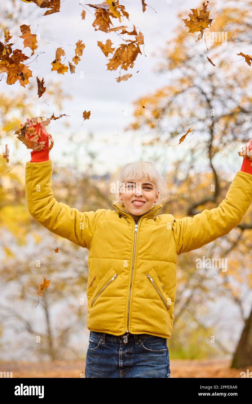 Jeune femme souriante jetant des feuilles d'automne Banque D'Images