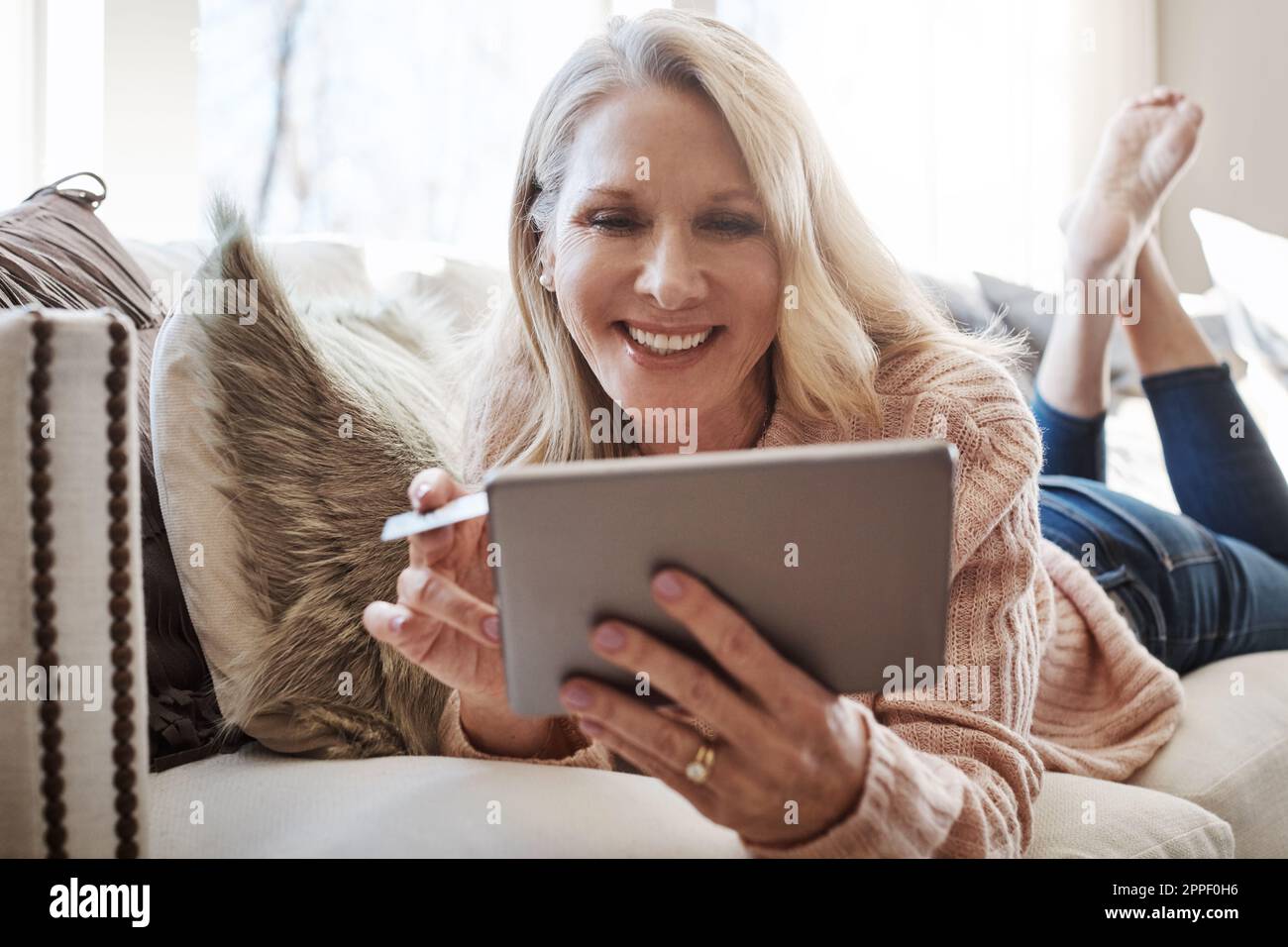 Confort et commodité grâce au crédit. une femme mûre utilisant une carte de crédit et une tablette numérique tout en se relaxant à la maison. Banque D'Images