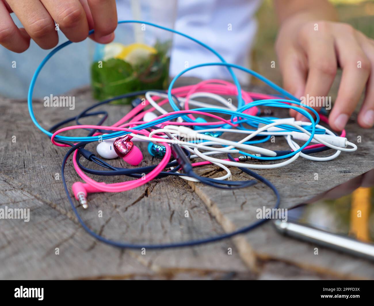 Les mains dénouent un nœud de quatre paires d'écouteurs intra-auriculaires filaires roses, bleus, blancs et noirs entremêlés dans un problème chaotique. Banque D'Images