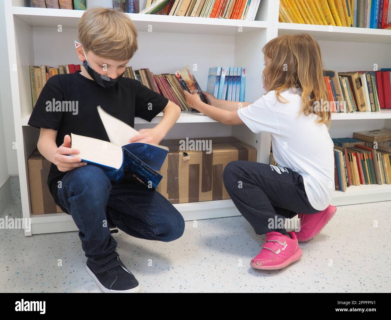 Sremska Mitrovica, Serbie, 15 mai 2021 enfants à la bibliothèque scolaire. Un garçon et une fille fouillent et feuillettent des livres dans le casier de la bibliothèque. Le garçon lit un livre très épais. Scolarisation. Les adolescents étudient Banque D'Images