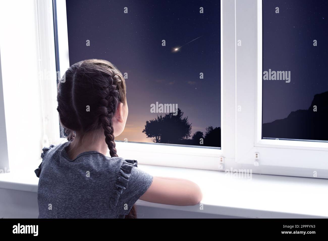 Petite fille mignonne près de la fenêtre et regardant l'étoile de tir dans le beau ciel de nuit Banque D'Images