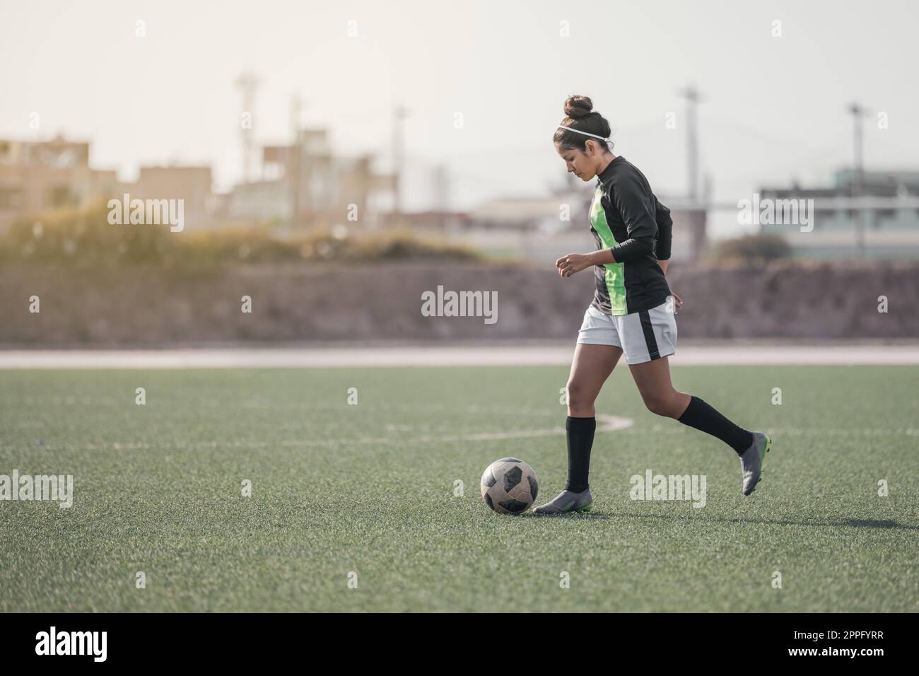 Jeune fille sur l'herbe botter un ballon de soccer et souriant Banque D'Images
