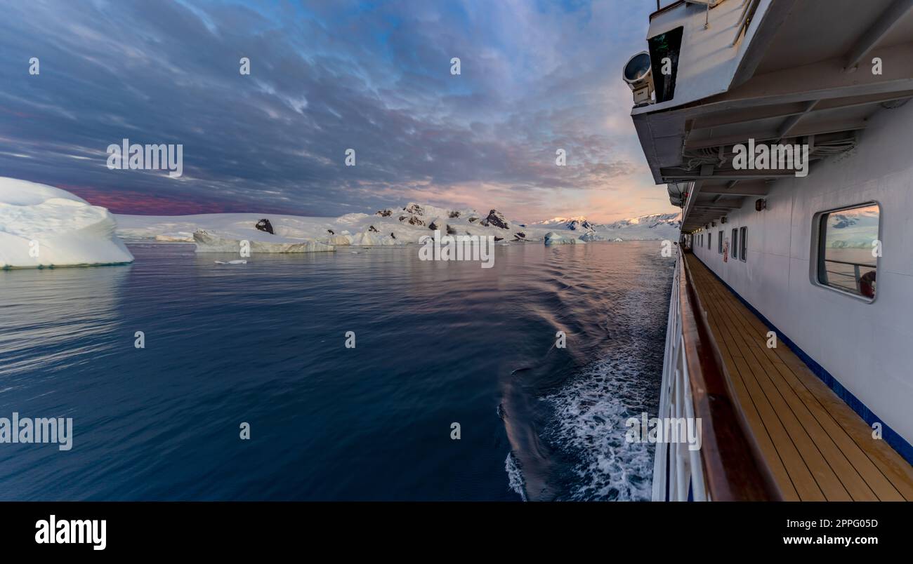 Bateau de croisière navigue à travers l'hiver Cierva Cove - une crique profonde sur le côté ouest de la péninsule Antarctique, entourée par la baie de Cierva dans la terre de San MartÃ­n - Antarctique, au cours d'un coucher de soleil dramatique / coucher de soleil du soir. Banque D'Images