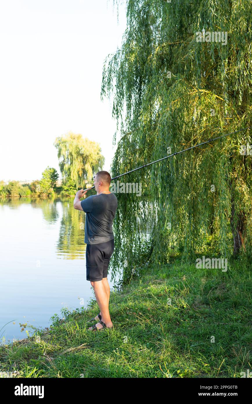 Moulinet de pêche. Le gars jette une canne à pêche contre le lac en toile de fond. Le concept de détente et de passe-temps pour l'âme. Banque D'Images